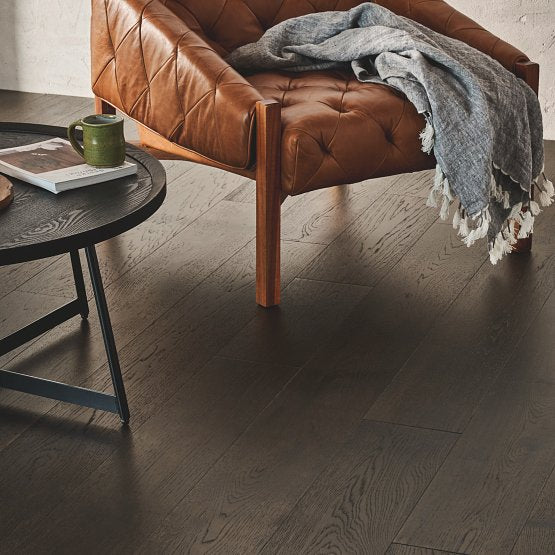 This is a room scene of the imperial pecan flooring in the color umber. There is a brown leather chair with a blanket hanging off of it