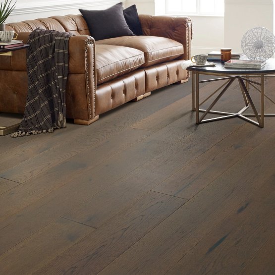 This is a picture of a living room with imperial pecan flooring with a brown leather couch and checkered blanket