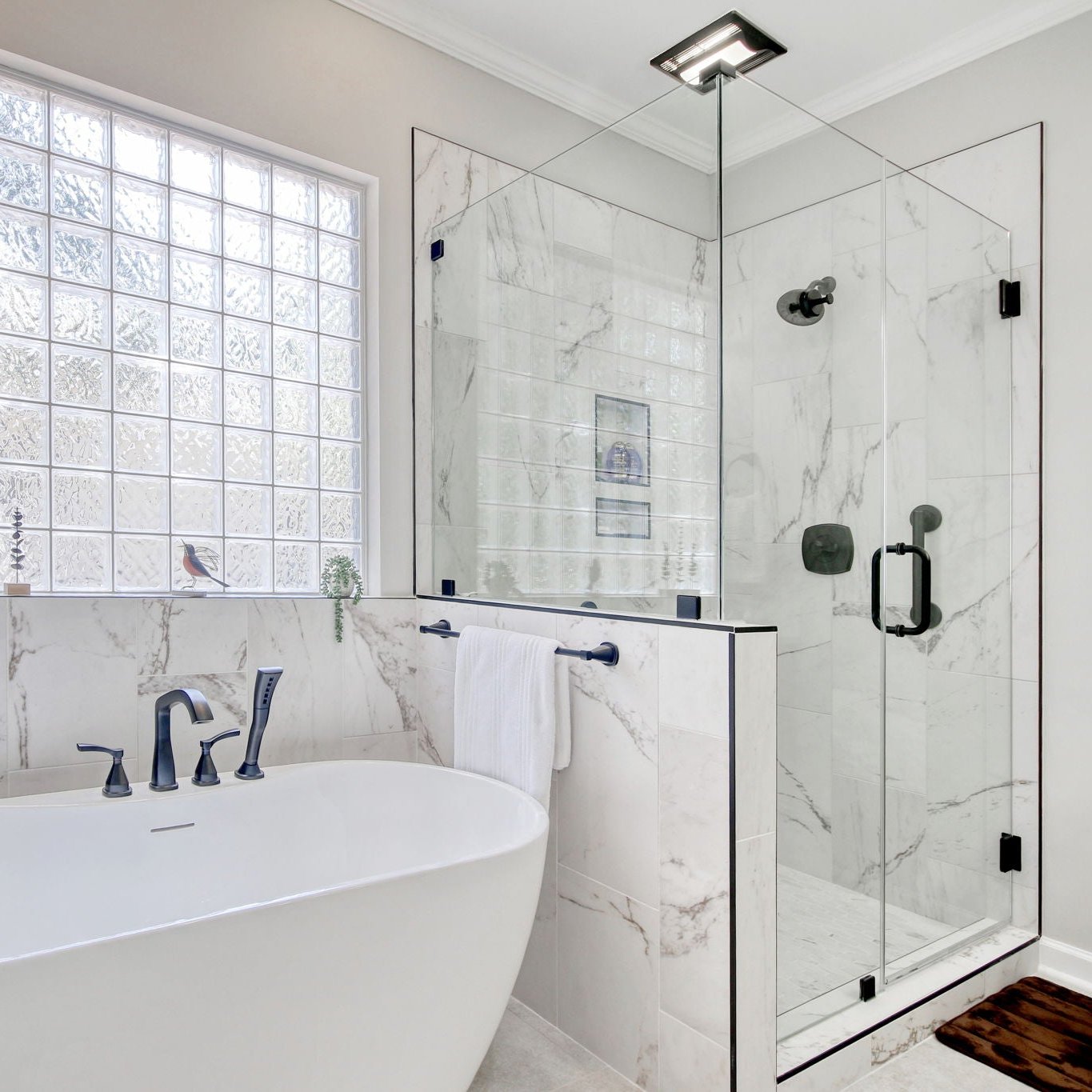 A bathroom scene with a floating tub and walk in tile shower. It is all marble tile with black hardware