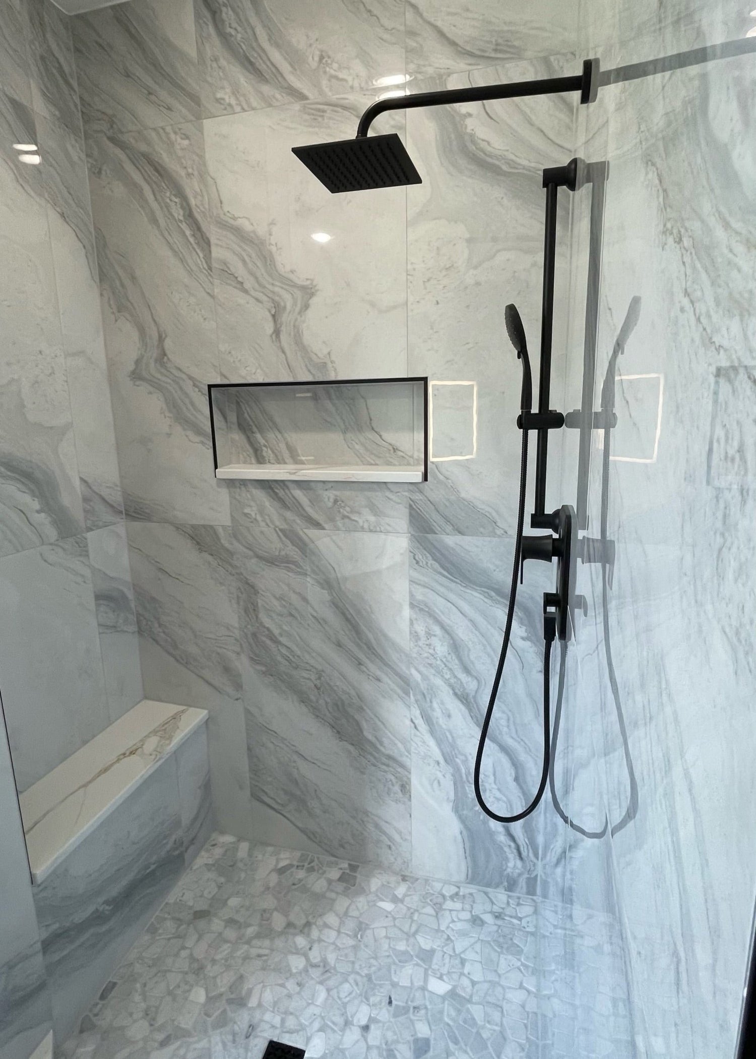 A tiled marble shower with black hardware and pebble flooring