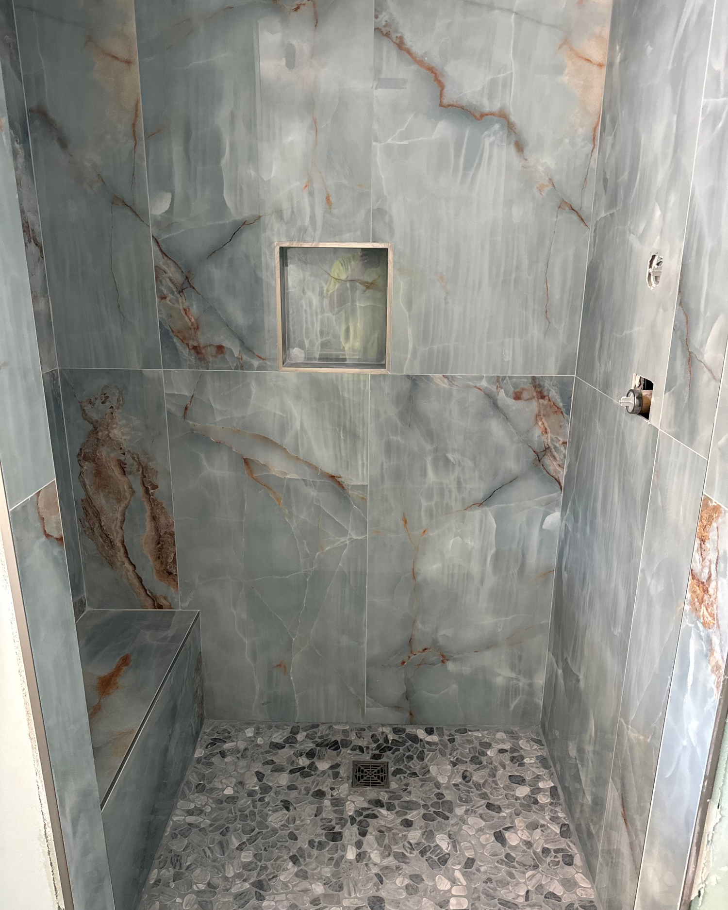 a tile shower with blue marble tile and pebbled shower floor