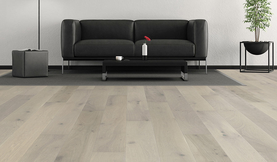 This is a room scene of palladio flooring in the color aspen. There is a black couch and a potted plant beside the couch
