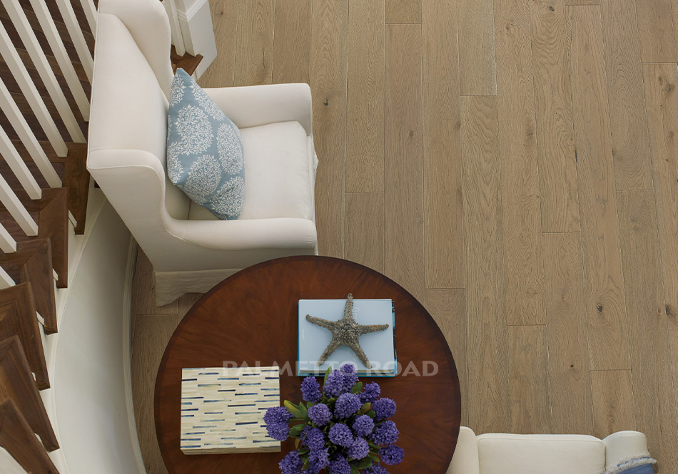 This is an aerial view of an entry way with the hardwood flooring monet in the color paris. There is a white colored chair with a wooden table positioned next to the staircase