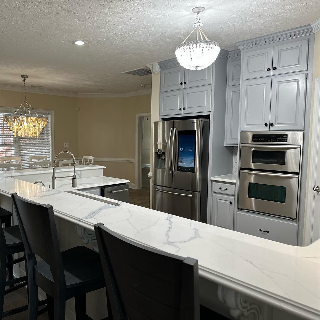 a kitchen with a marble table top and black charis. It has a double oven and grey cabinets
