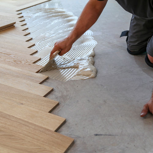 man laying hardwood floor with glue