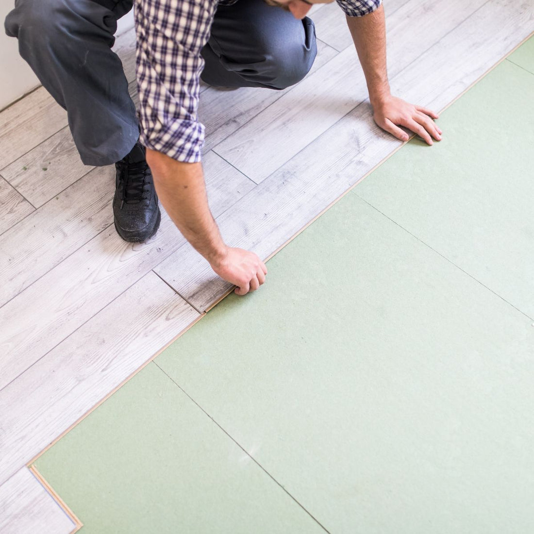 Man laying down lvp flooring. He is wearing jeans and a plaid shirt