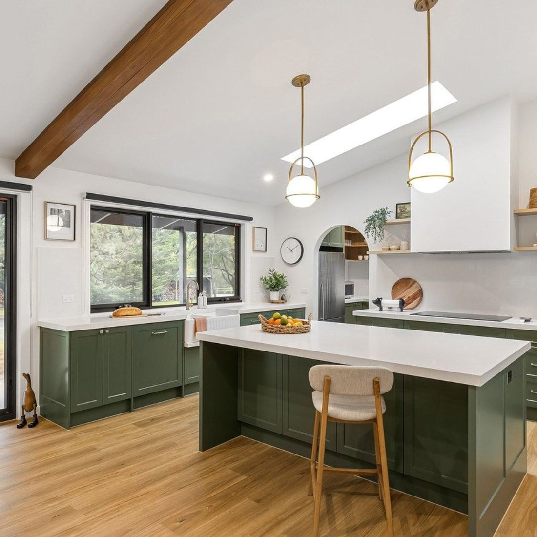 This is a kitchen scene with green cabinets and light warm wood flooring