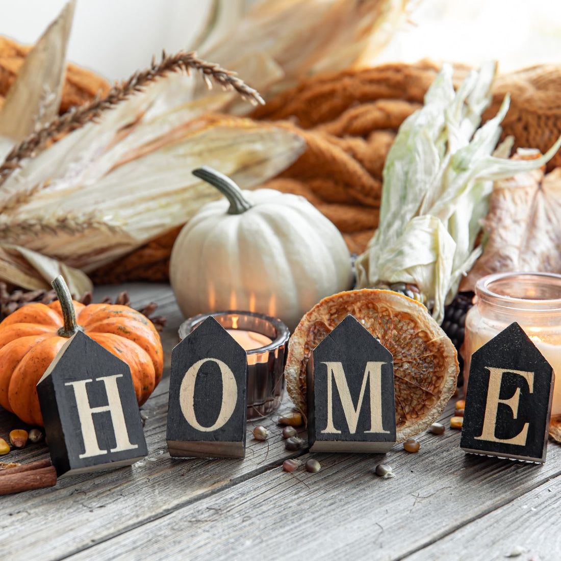 A sign that says home with white and orange pumpkins surrounding the sign