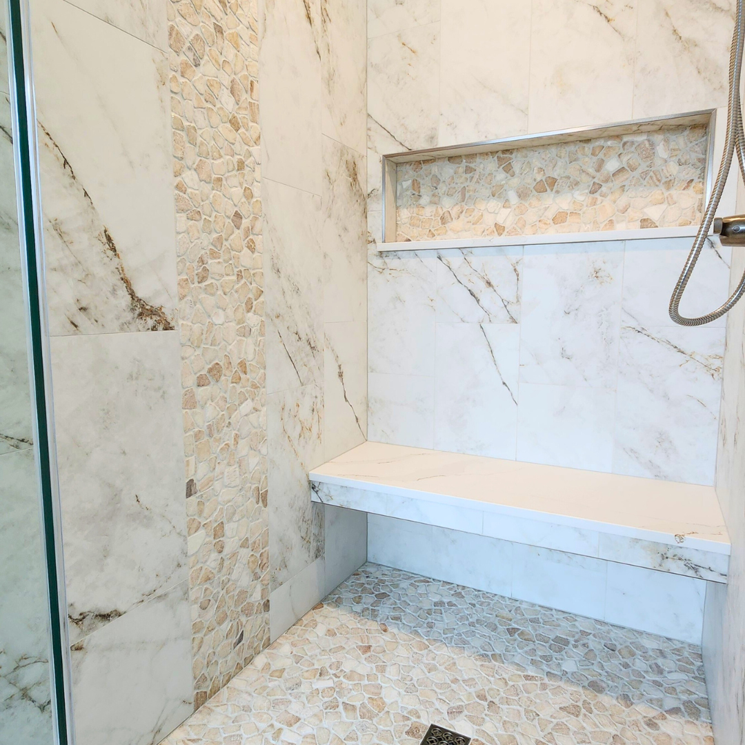 Modern shower with marble walls and floor, featuring a bench and shower head.