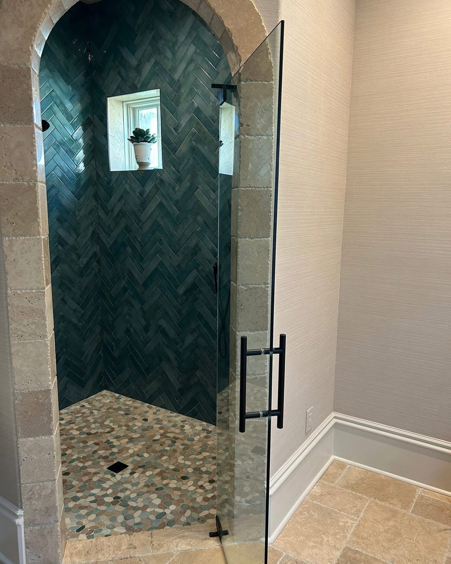 Glass shower enclosure with chevron patterned wall and pebble floor.