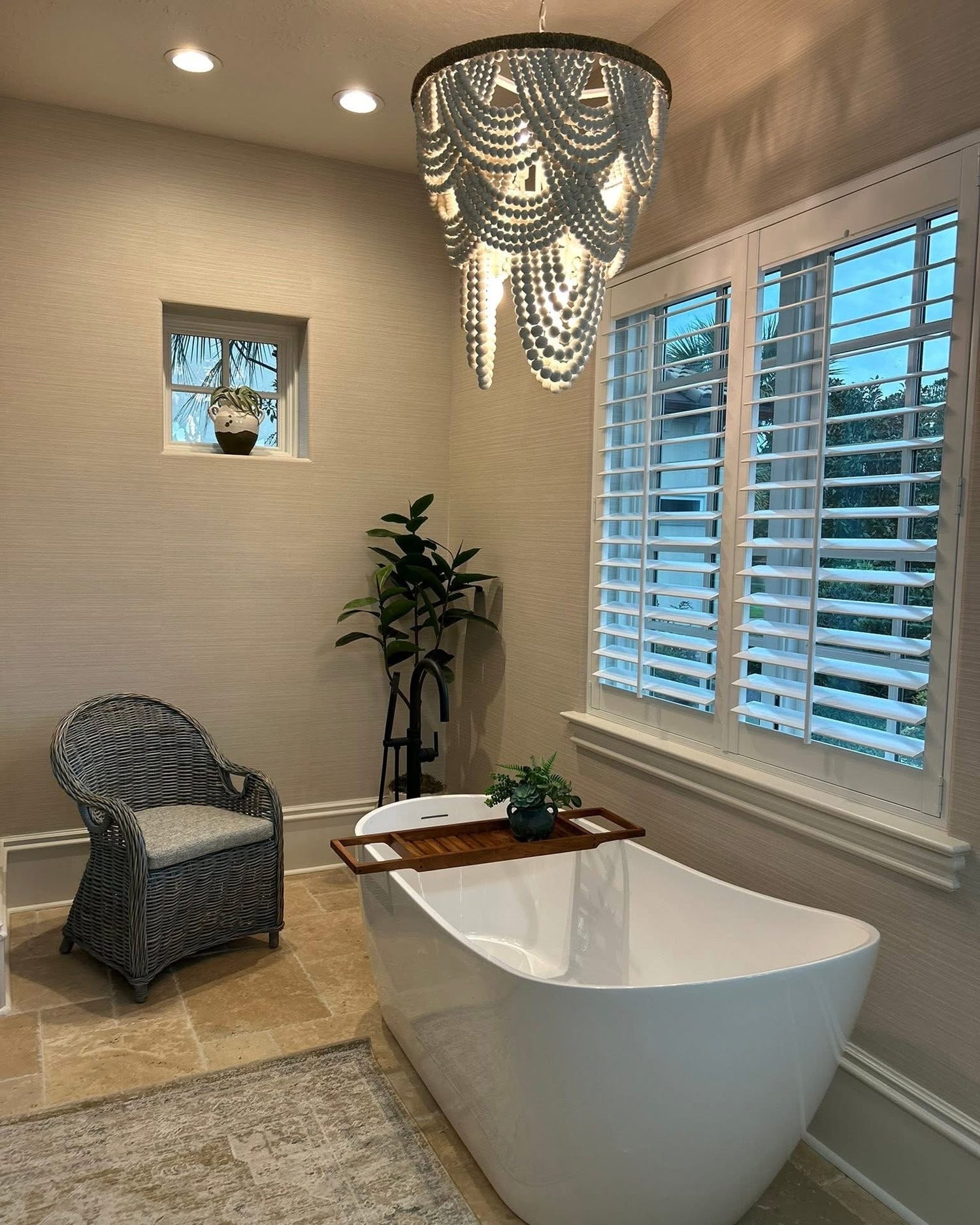 Modern bathroom with a freestanding bathtub, decorative chandelier, and a chair.