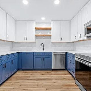 Modern kitchen with blue and white cabinets, stainless steel appliances, and wooden flooring.