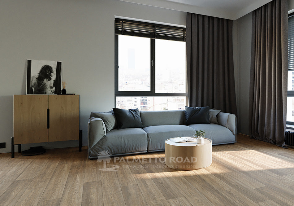 This is a room scene of a living room with a blue/grey couch and light colored wood furniture. The flooring is a laminate called trailblazer in the color teton crest