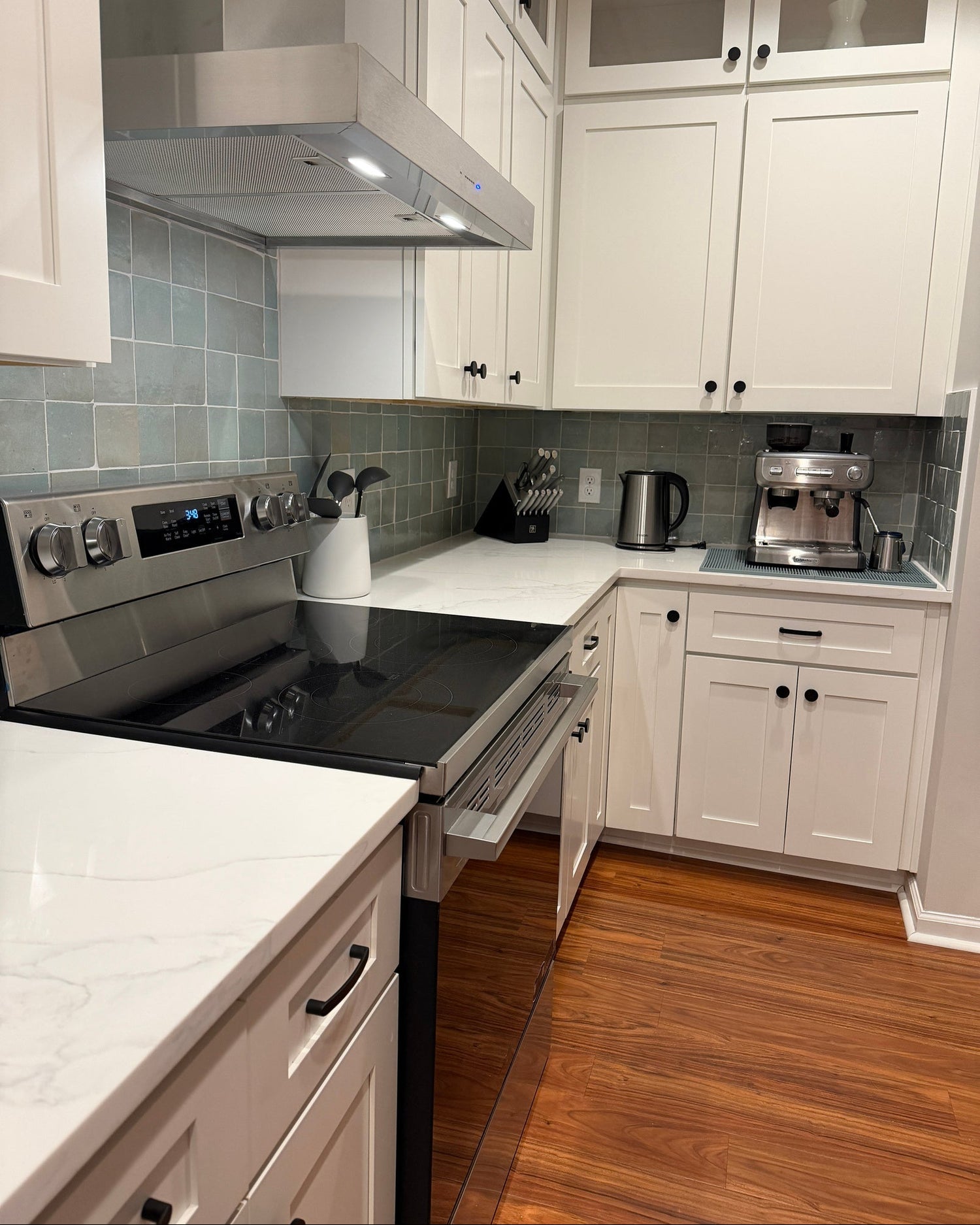 Modern kitchen with white cabinets, stainless steel appliances, and wooden flooring.
